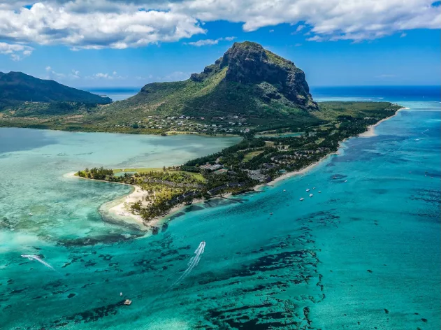 A view of an island in Mauritius, with azure blue ocean, clear blue skies and a lush green mountain.