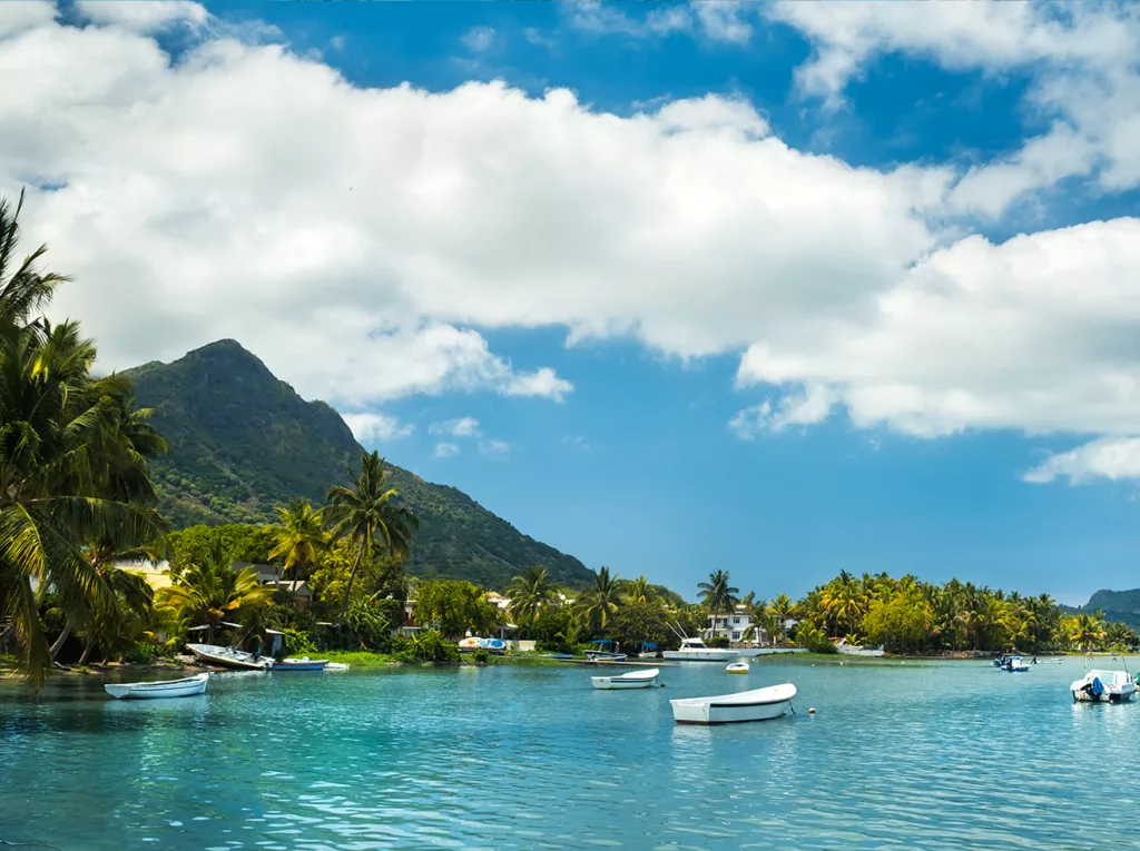 Boats rest peacefully on the ocean, with a mountain in the background.