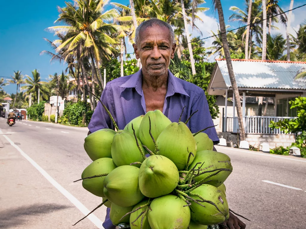 A man stands on a Mauritius road, holding coconuts for sale to tourists.