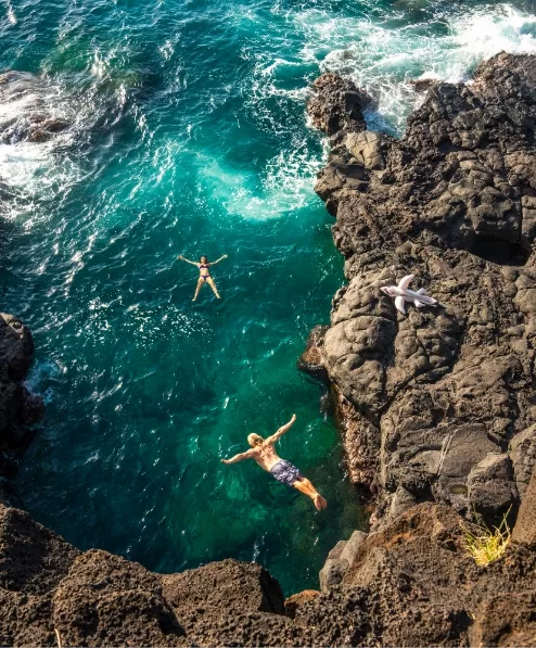 Two swimmers in an ocean cover surrounded by rocks and waves.